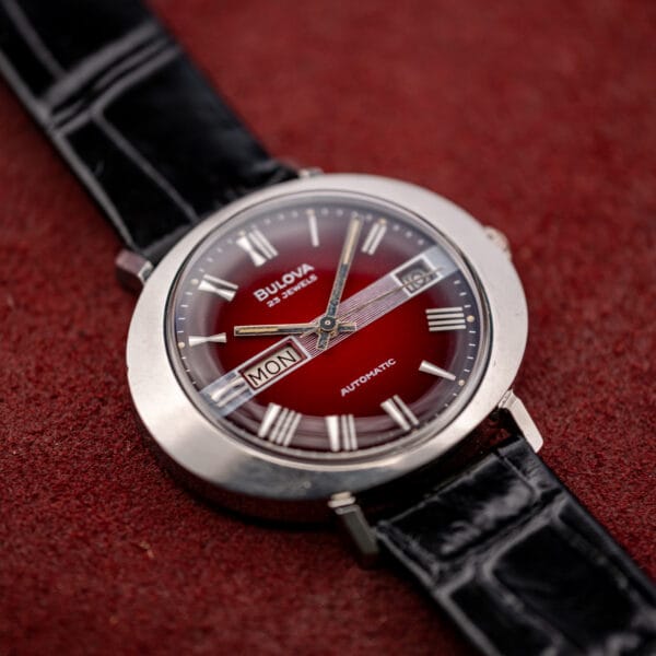 Bulova caliber 11 AOACB day/date from a low angle, crystal above the darkened maroon dial