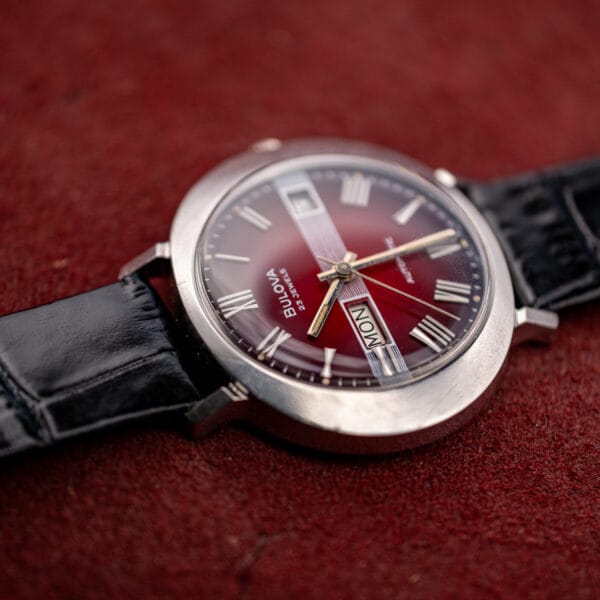 Bulova T-3092 rotated on velvet, day window at nine and the lined band crossing the maroon dial