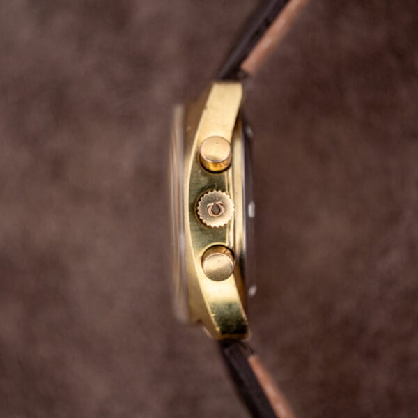 Omega 176.007 case flank in gold plate with two pump pushers flanking a signed Omega crown