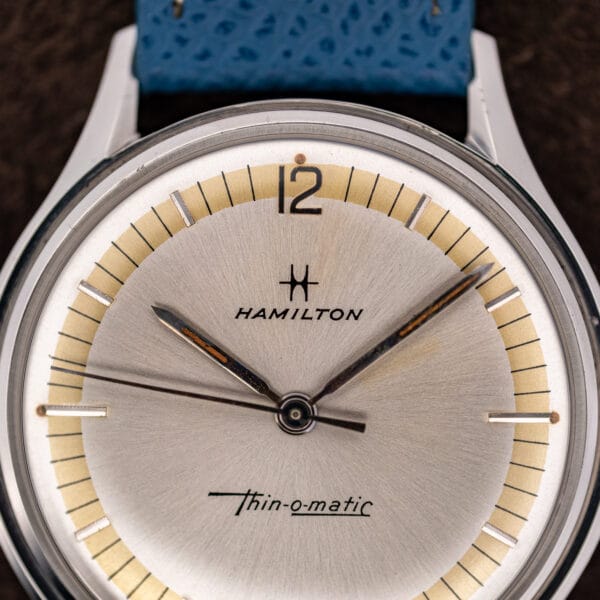 Hamilton Thin-O-Matic dial macro showing the H logo, open-outline 12 and combed champagne chapter ring