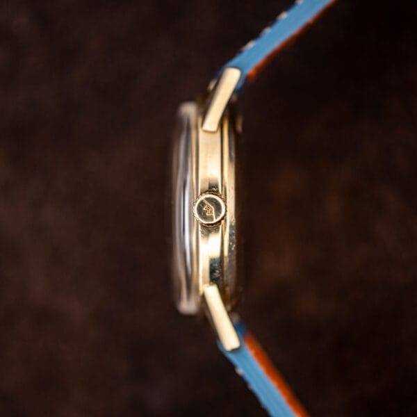 Close view of the Movado crown signed with the chevron logo beside the polished case