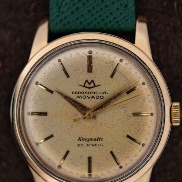 Movado Kingmatic dial macro reading CHRONOMETRE MOVADO above Kingmatic 28 JEWELS with heavy freckled champagne patina