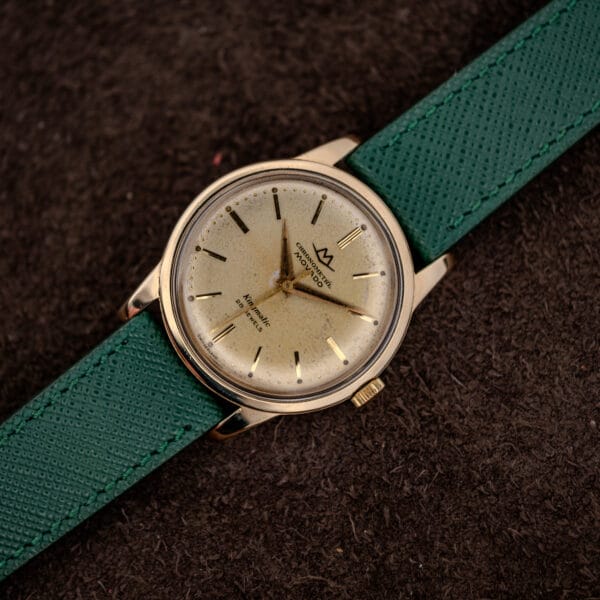 Movado Chronometre Kingmatic laid diagonally on a brown backdrop with faceted downturned lugs catching the light