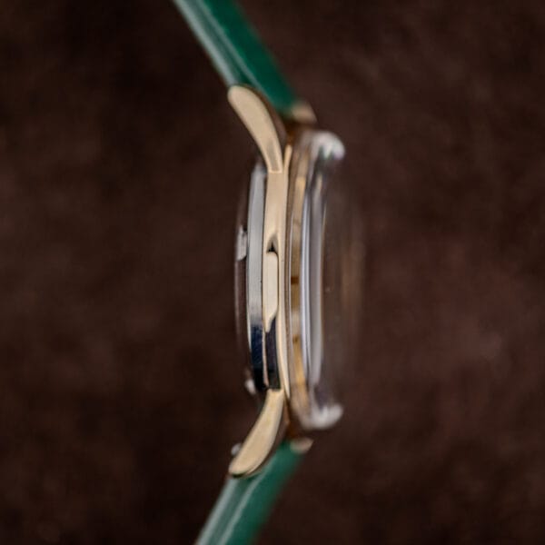 Movado Kingmatic side profile with domed acrylic crystal and gold capped case sitting over its polished steel back