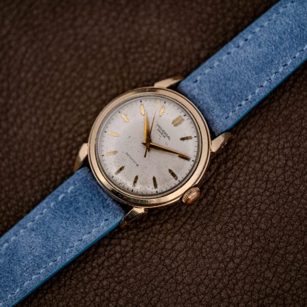 The full watch and its powder blue strap laid at an angle across dark brown leather