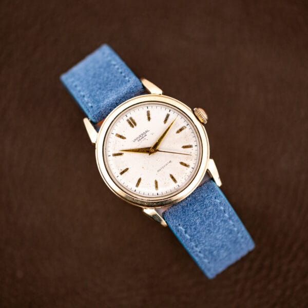 Overhead view of the complete watch and suede strap on a brown leather ground