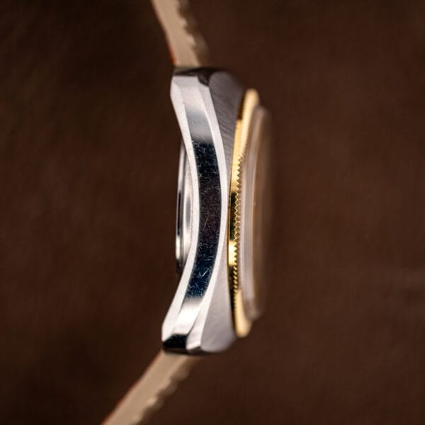 Side profile showing the slim cushion case, fine bezel fluting and taupe saffiano strap