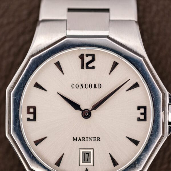 Close view of the silver sunburst dial, black wedge markers and squared numerals at twelve, three and nine