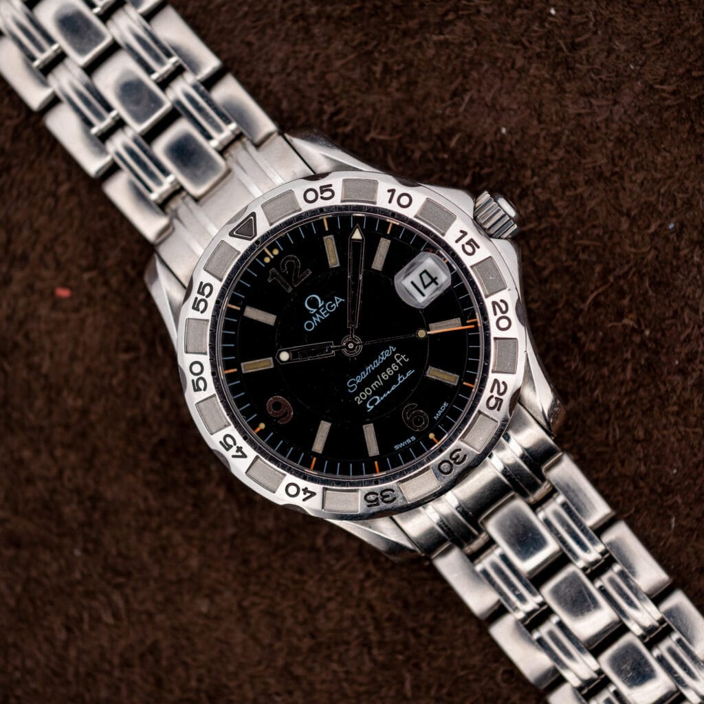Vintage Omega Seamaster Autoquartz 196.1526 seen from above, black wave dial and steel bracelet on brown suede.