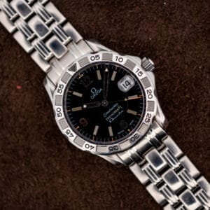 Vintage Omega Seamaster Autoquartz 196.1526 seen from above, black wave dial and steel bracelet on brown suede.