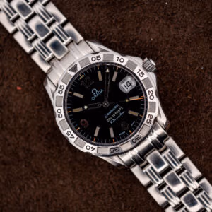 Vintage Omega Seamaster Autoquartz 196.1526 seen from above, black wave dial and steel bracelet on brown suede.