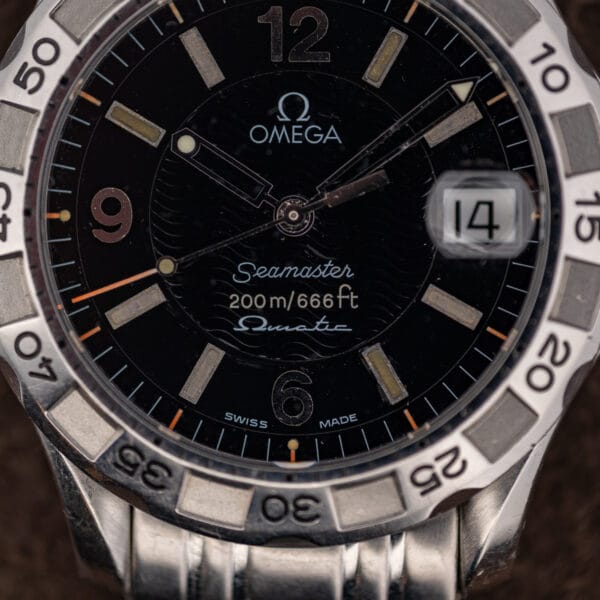 Full dial macro of the Seamaster Autoquartz showing Swiss Made printing, orange minute track and cream aged lume.