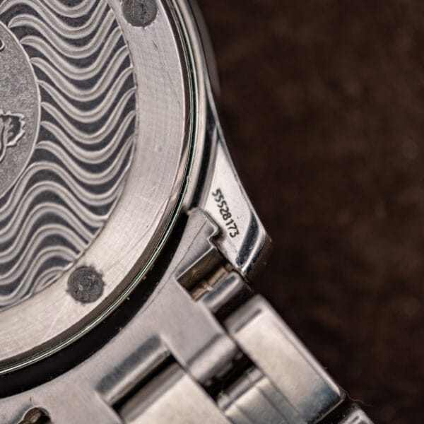 Macro of the caseback edge and lug engraving showing Omega case serial number 55528173 between the wave lines.