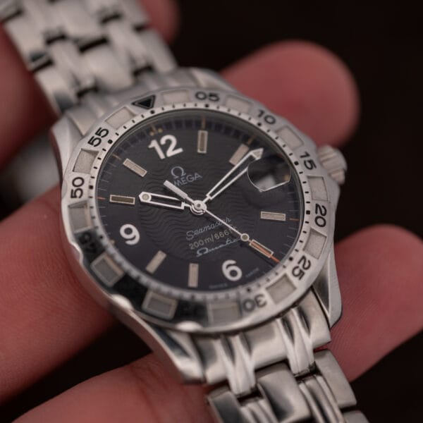 Omega Seamaster 200M held between fingers, showing case proportions and the black dial in natural light.