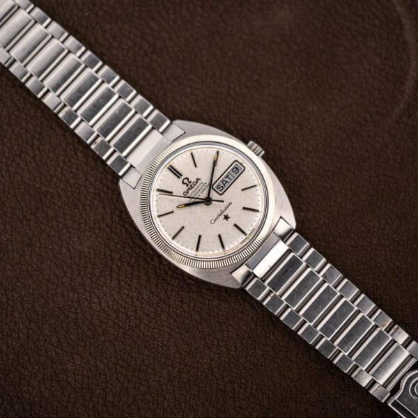 Vintage Omega Constellation watch and Omega steel bracelet laid diagonally across a brown leather surface