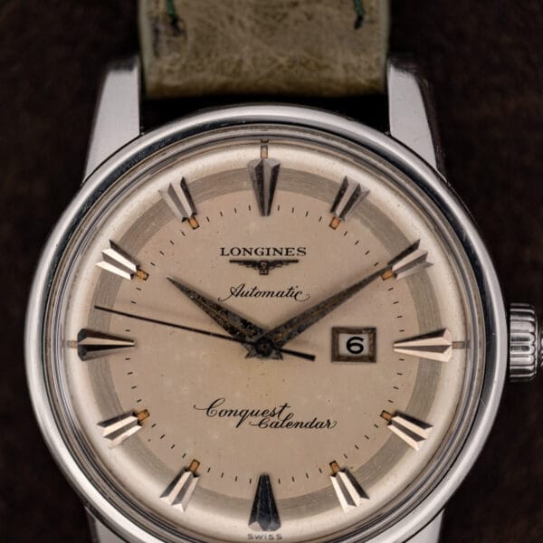 Cream Conquest Calendar dial macro: winged hourglass logo, script model name, framed date window at three