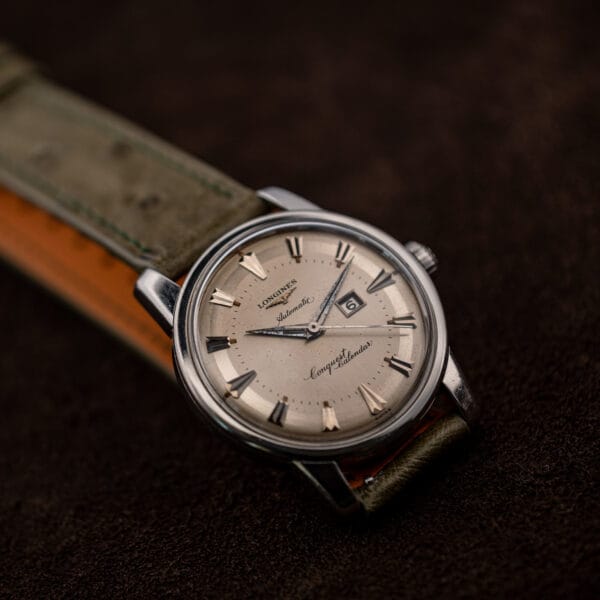 Tilted view of the Conquest Calendar dial, fluted crown and the strap's dark green saddle stitching