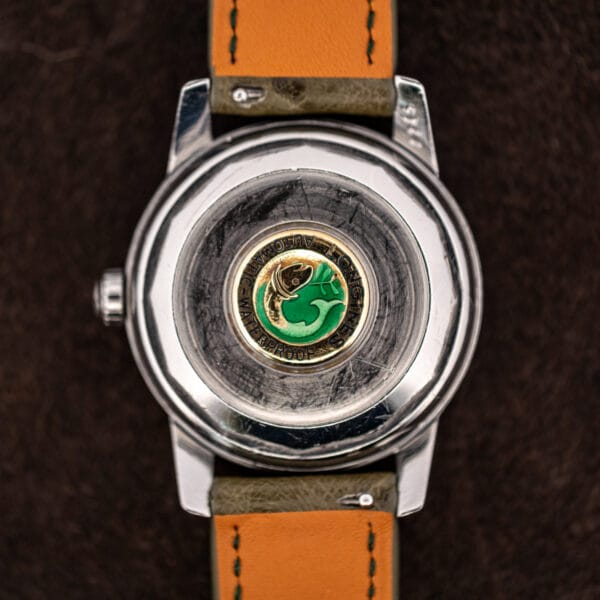 Conquest caseback medallion, green enamel fish in a gilt ring marked Longines Automatic Waterproof, surrounded by scratching