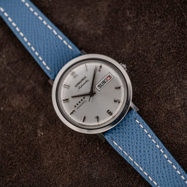 Overhead angled shot of the Longines Admiral automatic, full case shape and silver sunburst dial on blue leather
