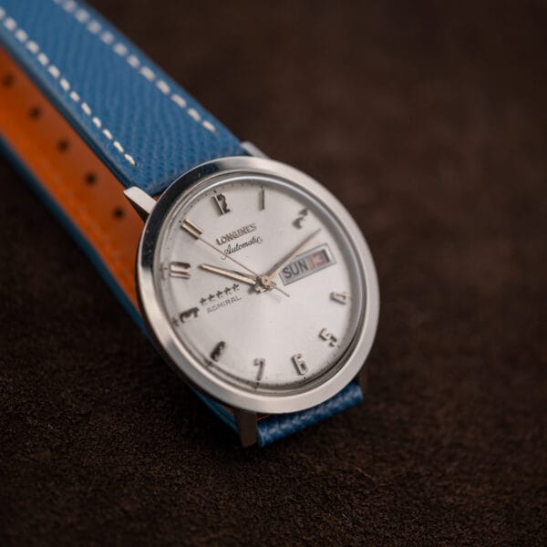 Styled angle of the Longines Admiral with the strap tail folded to show punched adjustment holes and orange lining