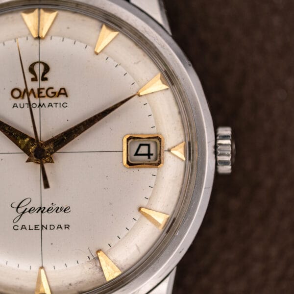 Omega 2982-3 SC tarnished gold-tone date frame at three reading 4, with fluted steel crown alongside