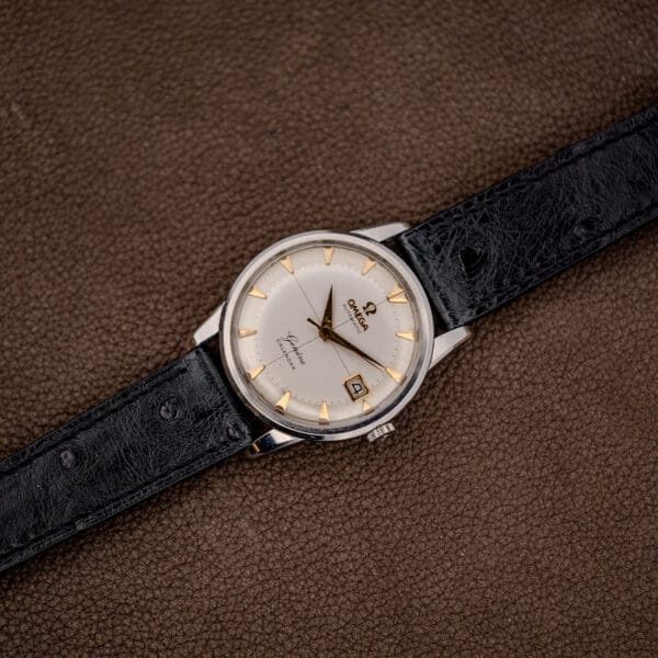 Full Omega 2982-3 SC wristwatch overhead with black ostrich leather strap extended across a brown leather surface