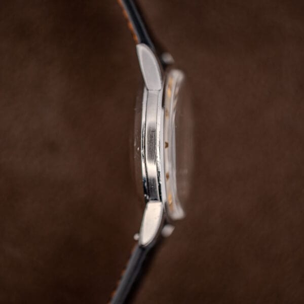 Smooth unmarked nine o'clock flank of the Omega Geneve Calendar case, confirming a single crown and no pushers