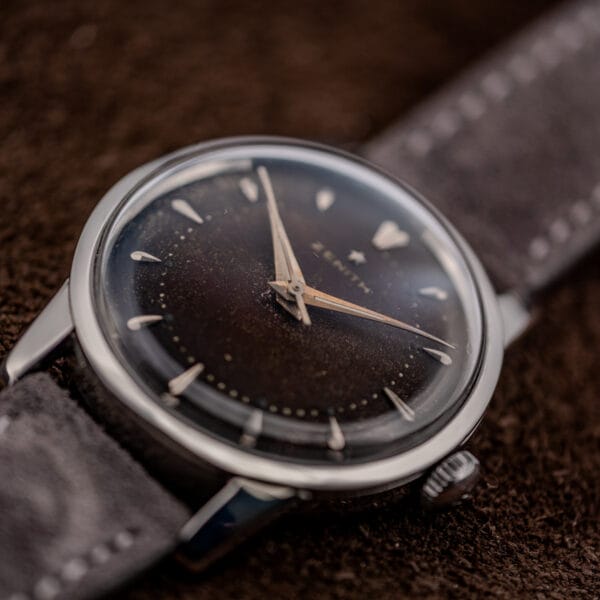 Low angle across the domed crystal of a vintage Zenith showing bezel profile and dark browned dial