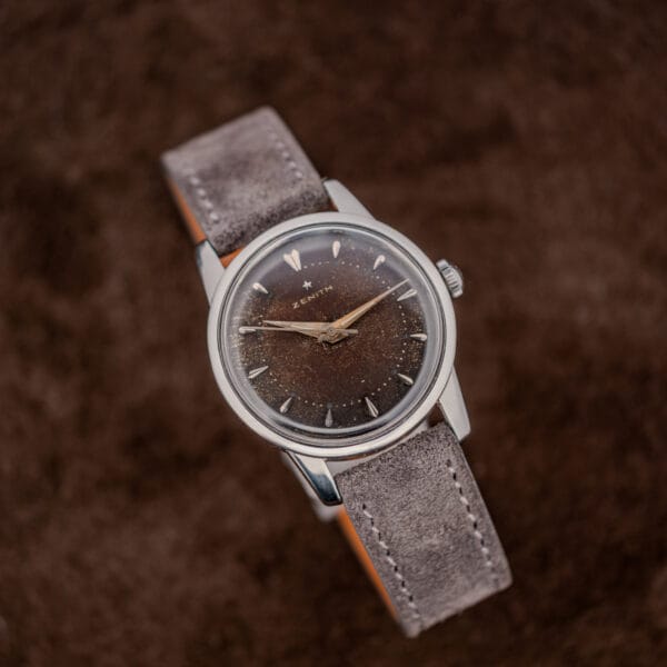 Complete vintage Zenith wristwatch laid out with its anthracite Italian suede strap on a brown suede surface