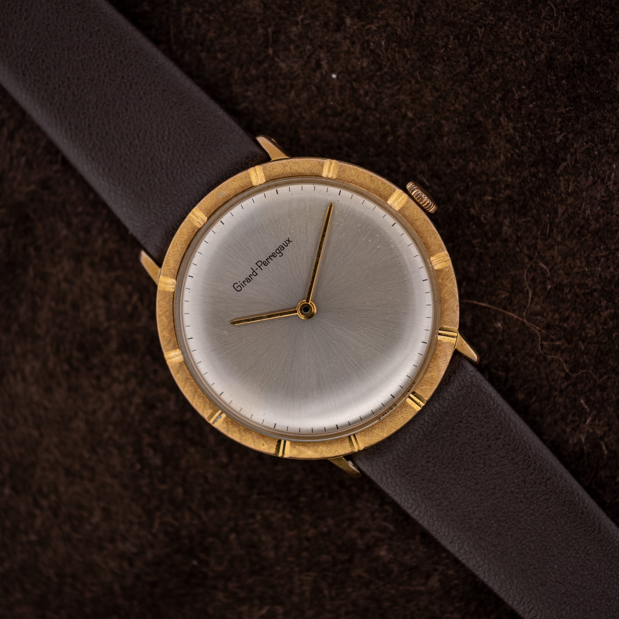 DSCF6570 Girard-Perregaux silver sunburst dial, two gold-toned hands, and a textured bezel with twelve polished notches, shown on suede
