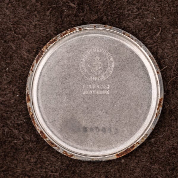 Inside the removed Girard-Perregaux caseback, embossed brand roundel above the stainless steel stamping, with rust around the rim