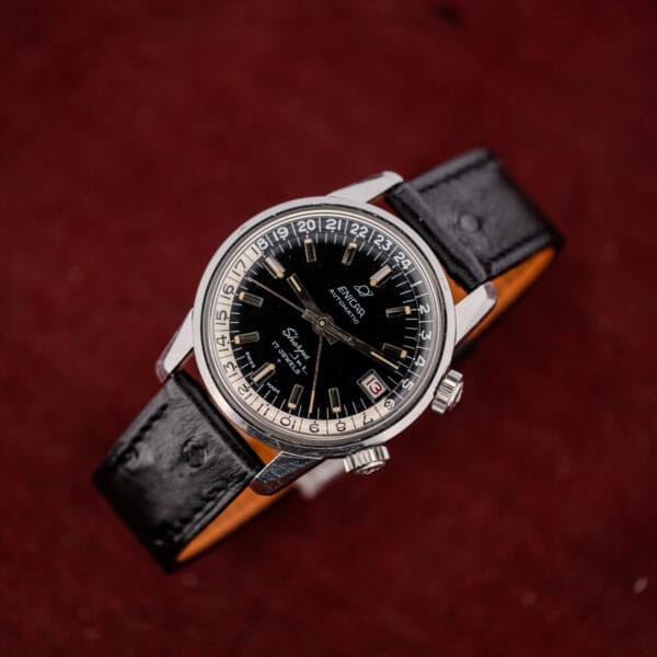 Complete vintage Enicar Sherpa Jet with its black ostrich pattern strap laid out on deep red suede