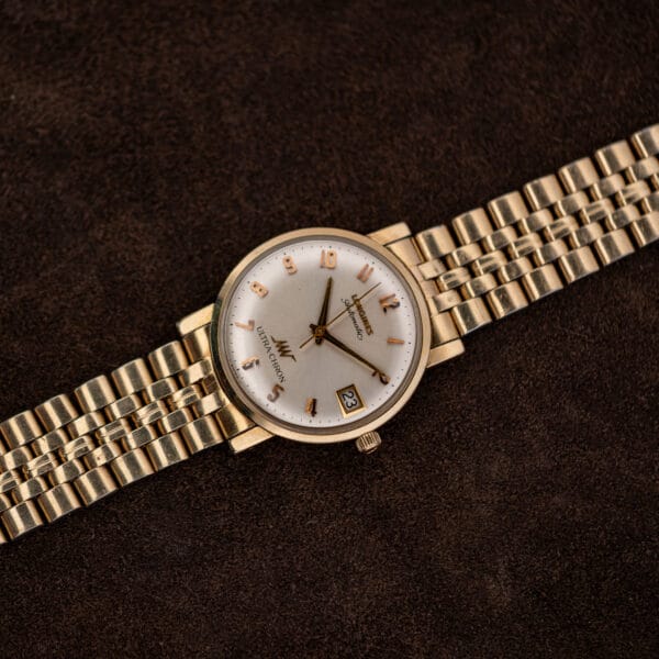 Full overhead view of the Longines Ultra-Chron automatic with its gold-tone bracelet laid flat on brown suede