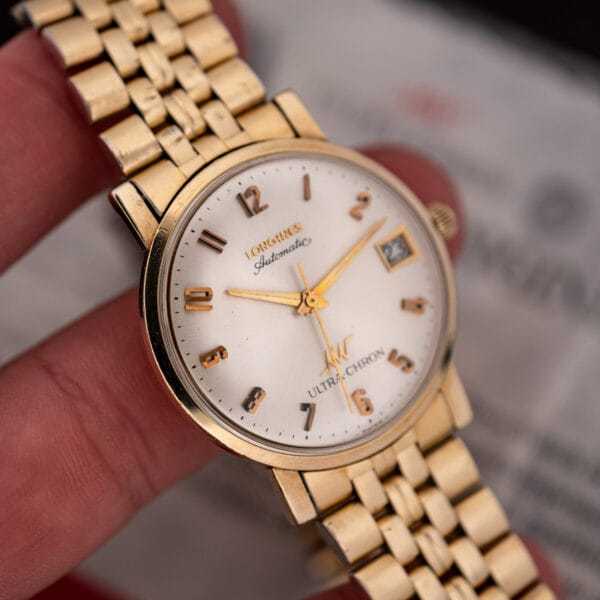 Longines Ultra-Chron held in hand showing applied rose gold numerals and date window, certificate blurred behind