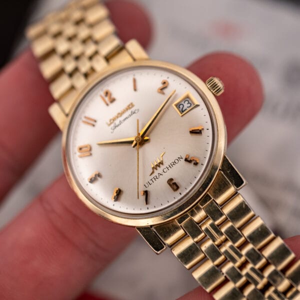 Close in-hand view of the Longines Ultra-Chron dial signature, date aperture and worn gold filled case edge