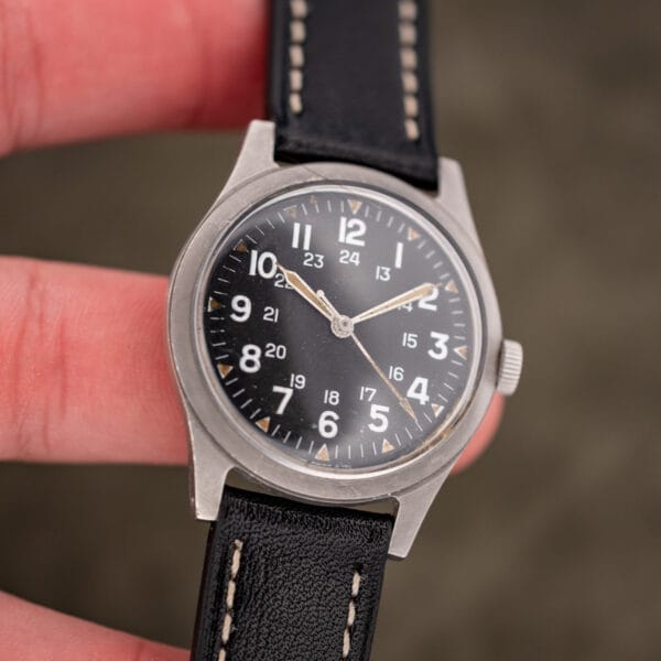 Vintage Benrus GG-W-113 military watch held in hand for scale, showing dial speckling and cracked hand lume