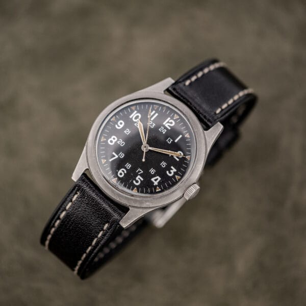 Overhead view of the Benrus GG-W-113 with black leather strap laid open and sterile 24 hour dial