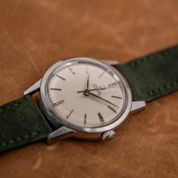 Angled view of Omega 14773-1 white dial, applied batons and slim central seconds hand under domed acrylic crystal