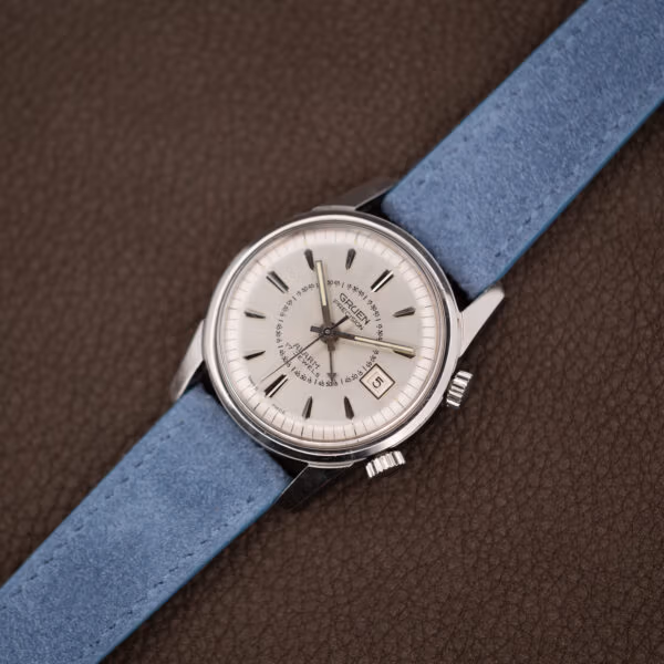 Vintage Gruen alarm watch angled on light blue suede, aged cream lume plots around the minute track