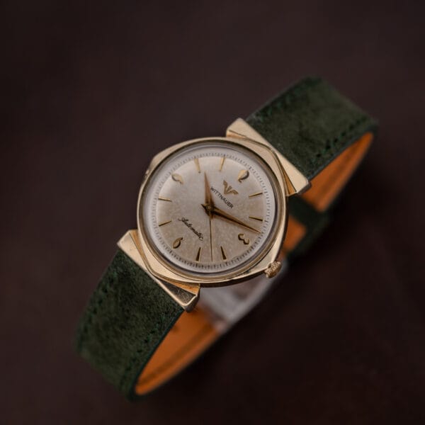 Hooded lug case in gold tone, speckled silver dial and gold Arabic numerals against green suede