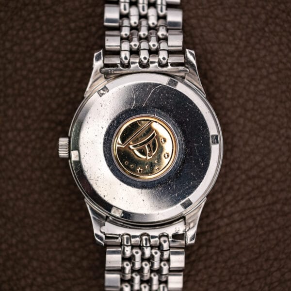 Omega Constellation 14393 steel caseback with gold-tone observatory medallion, deep scratches and perimeter tool notches
