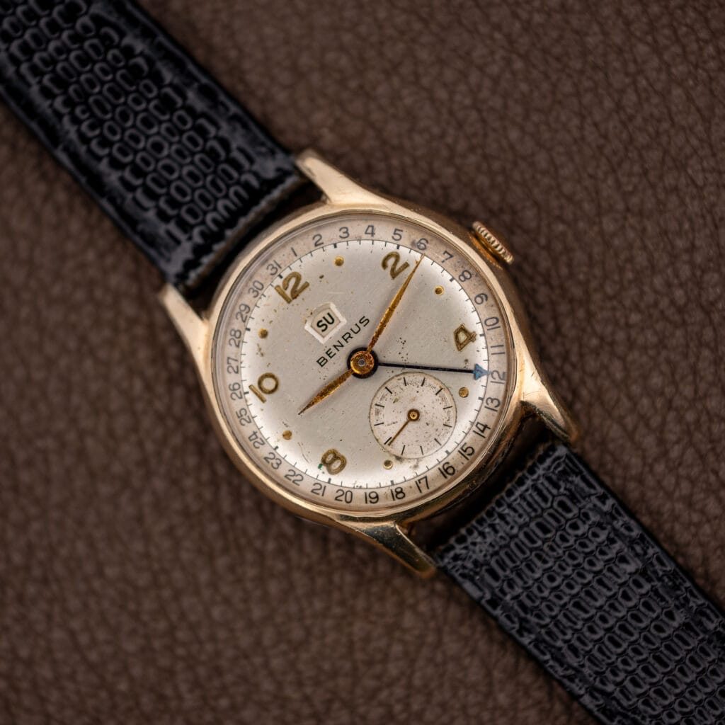Vintage Benrus pointer date and day wristwatch, white Arabic numeral dial, black leather strap, angled front view