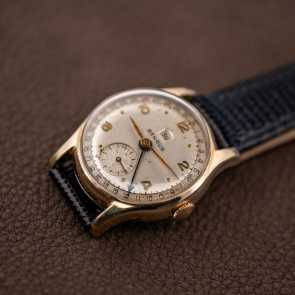 Benrus calendar wristwatch at an angle showing the day aperture, blued pointer date hand and tarnished applied numerals