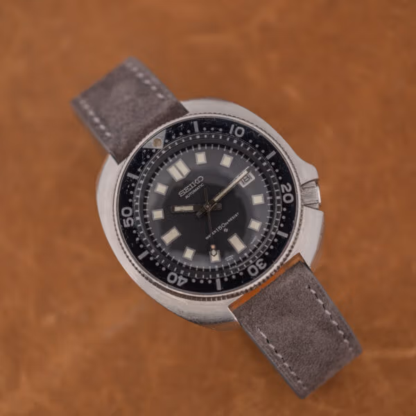 Angled Seiko 6105-8119 diver showing aged hands, faded bezel pip and anthracite suede strap