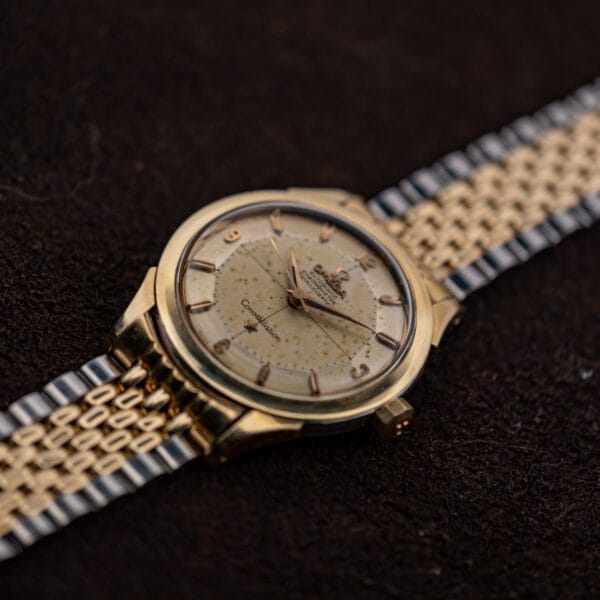 Angled macro of Omega Constellation 2852-9 SC dial with applied markers and Arabic numerals on a spotted cream surface