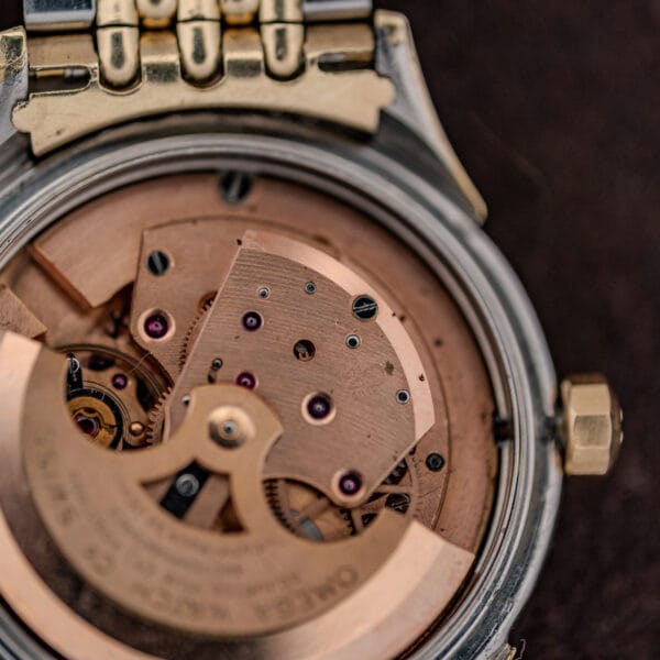 Macro of Omega cal. 505 movement bridge stamped 505 beside faceted crown and copper toned plates