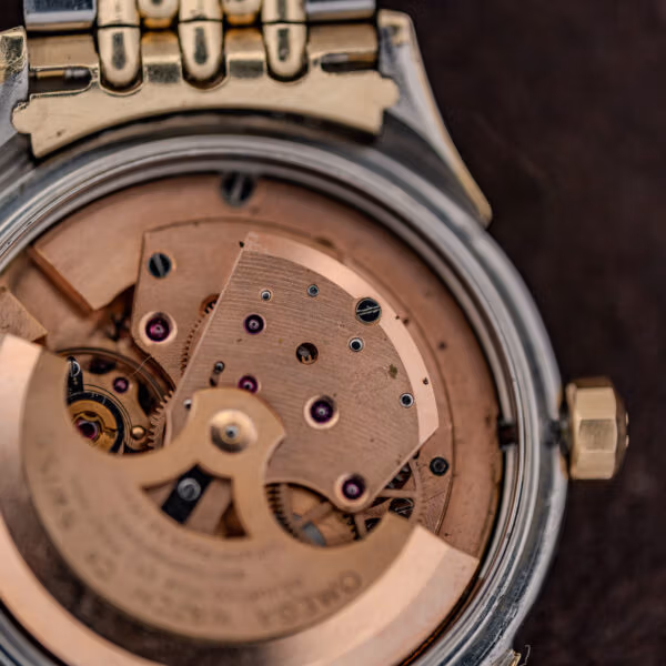 Macro of Omega cal. 505 movement bridge stamped 505 beside faceted crown and copper toned plates