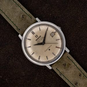 Omega Constellation 168.004 resting diagonally on brown fabric with its silver dial and olive ostrich strap