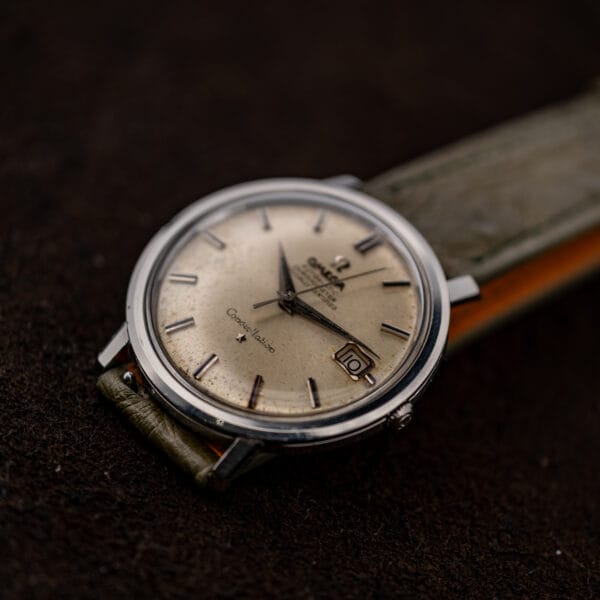 Three-quarter view of Omega Constellation 168.004 with date window foreground and olive strap extending upward