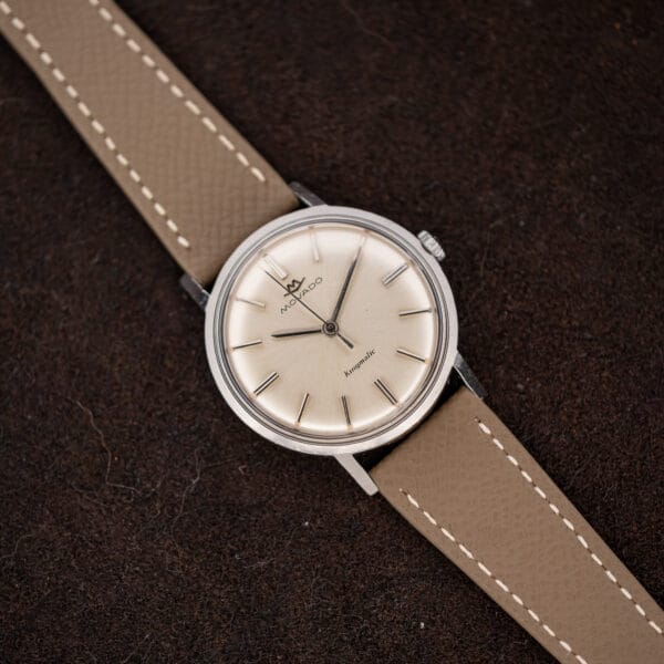 Overhead Movado Kingmatic 15161 with its taupe Saffiano leather strap extended across the dark fabric background